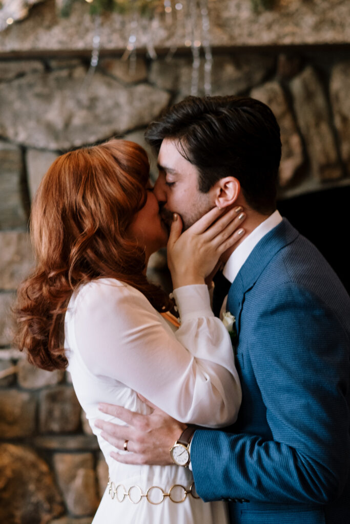 Bride and groom kissing in front of fireplace during winter New England elopement