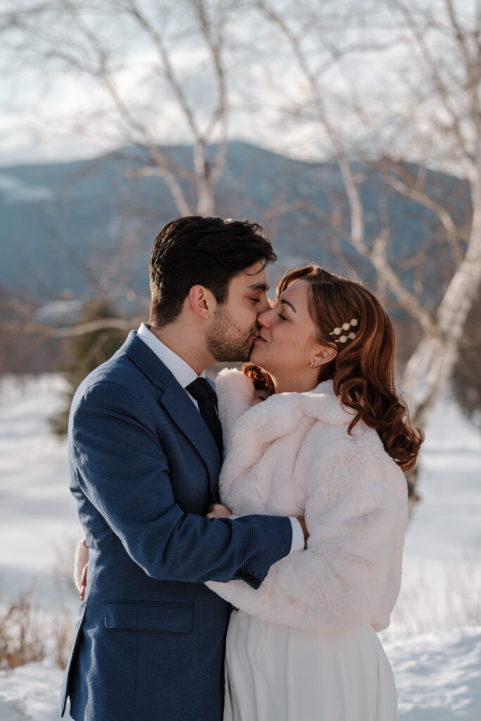 Couple kissing outside in the snow during winter elopement in the White Mountains