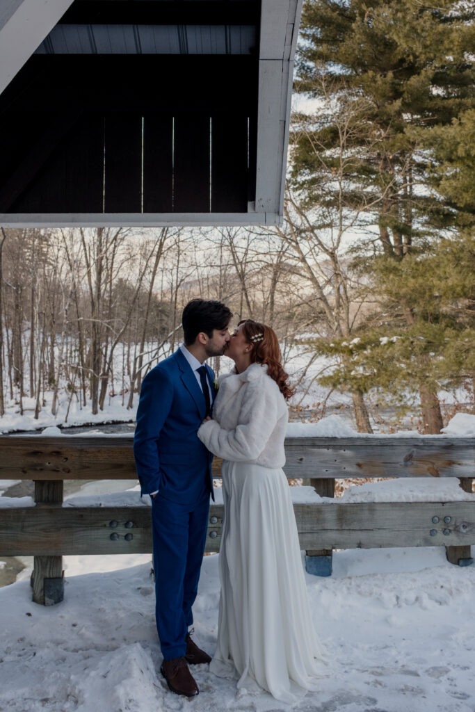 Bride and groom on covered bridge during winter elopement in the White Mountains